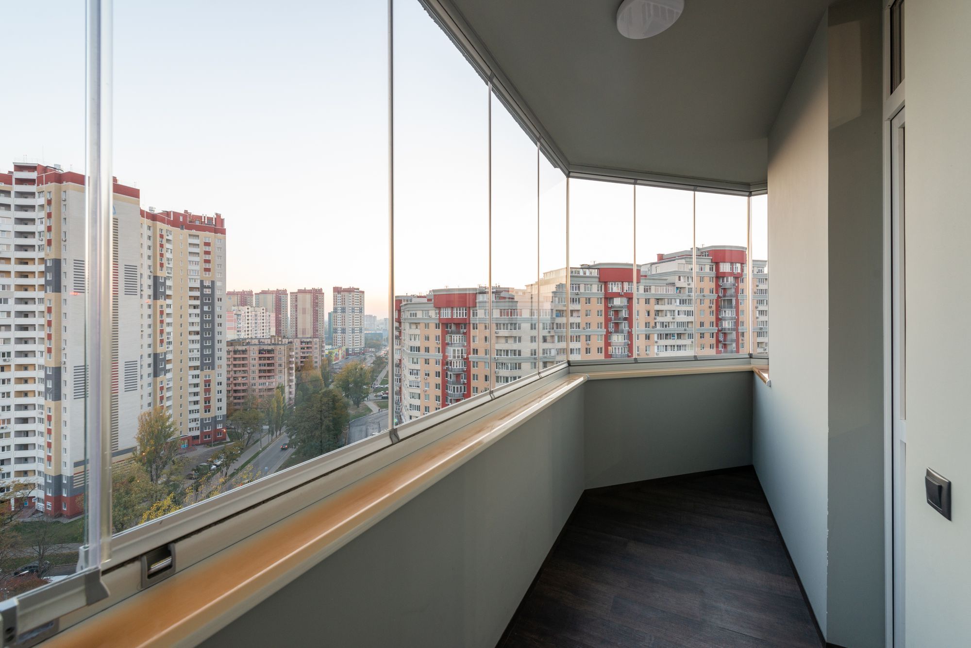 Sacada de apartamento fechada com cortina de vidro sem perfis verticais, com vista para prédios da cidade